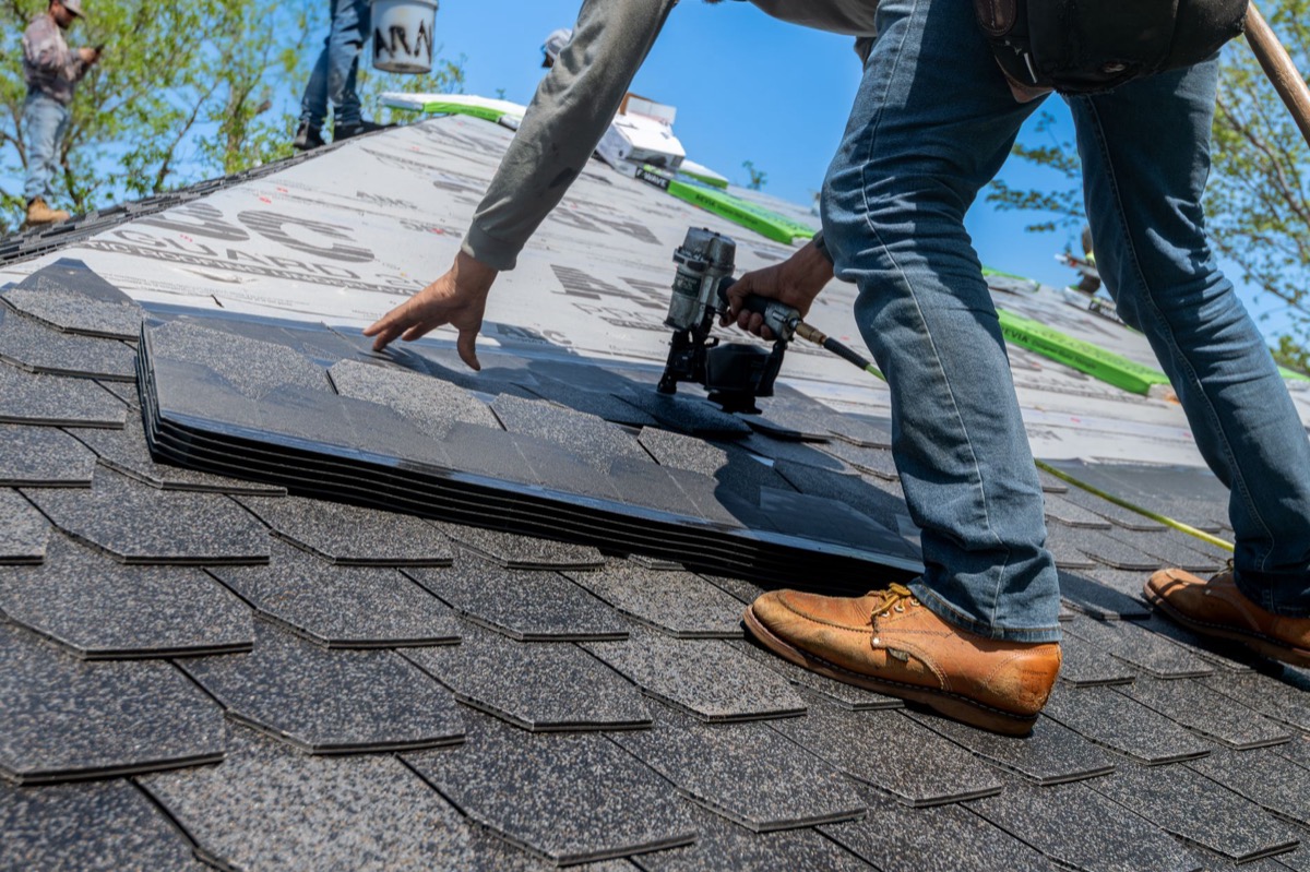 Roofer nailing asphalt shingles on a steep residential roof on a sunny day